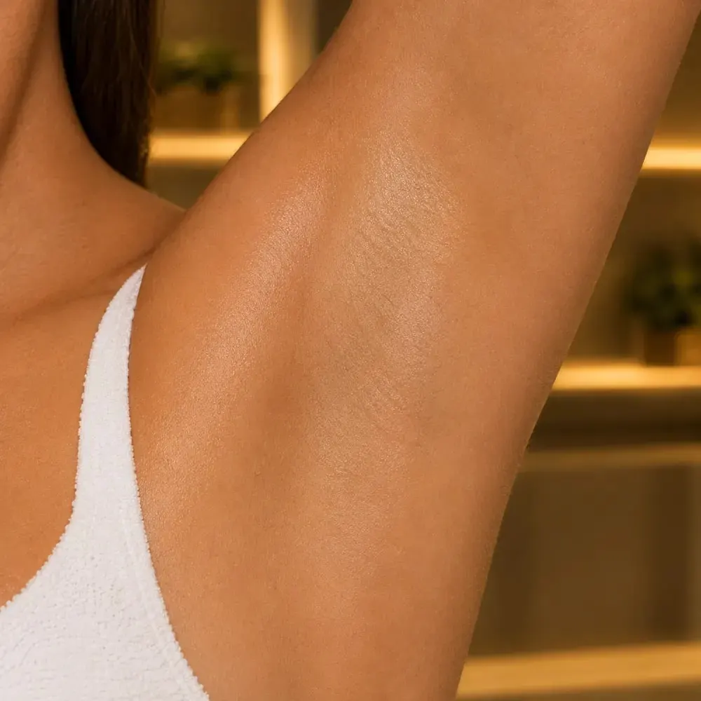 Axila feminina com pele lisa e uniforme em ambiente de clínica com luz dourada